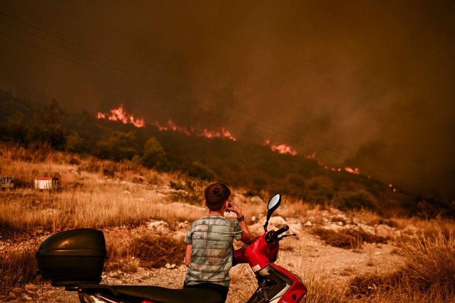 Menino observa um incêndio florestal em Chasia, nos arredores de Atenas, em 22 de agosto de 2023.