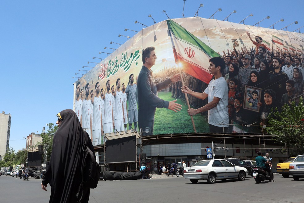Mulher iraniana passa por outdoor em apoio à seleção nacional de futebol do Irã para a Copa do Mundo de 2026, em Teerã — Foto: AFP