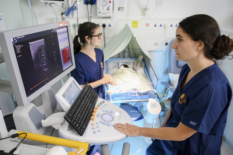 Dra. Flora Faure (&agrave; direita) e a Dra. Sara de Crescenzo realizando um exame em um beb&ecirc; prematuro para obter imagens do c&eacute;rebro inteiro e observar a atividade neural, em Cambridge, Inglaterra &mdash; Foto: Joel Frohlich/Hospital Universit&aacute;rio de T&uuml;bingen via The New York Times