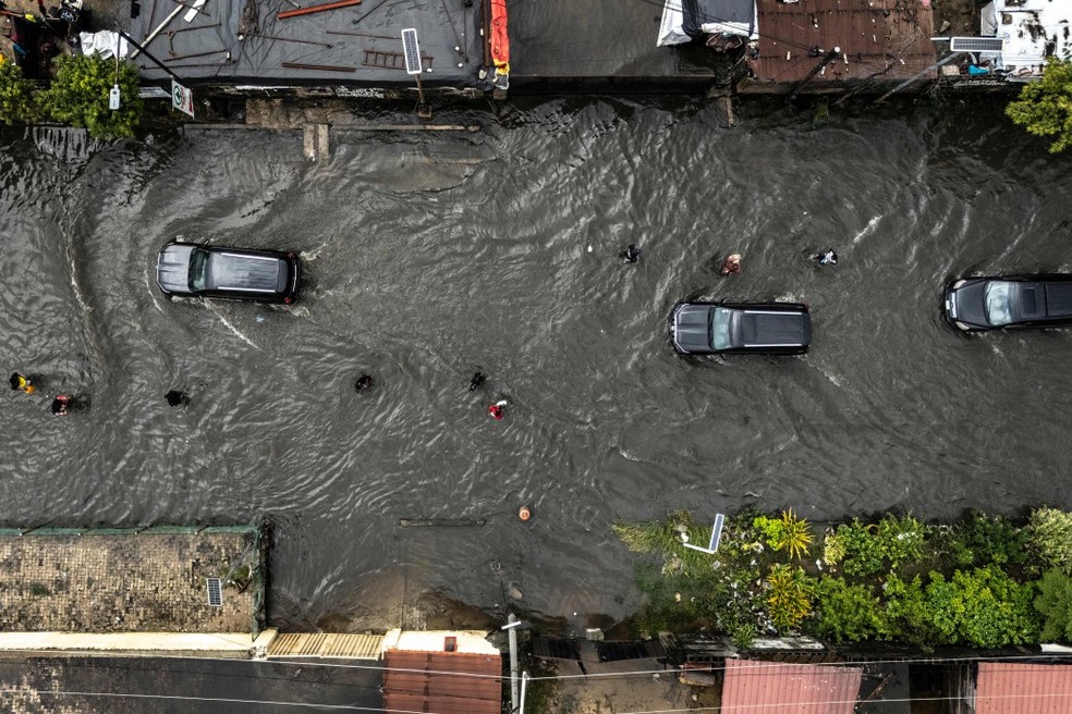Esta vista aérea mostra carros trafegando e pedestres caminhando por uma rua alagada no bairro de Lekki, em Lagos, em 3 de julho de 2026. Lagos está entre as cidades costeiras que mais sofrem os impactos das mudanças climáticas na costa da África Ocidental — Foto: OLYMPIA DE MAISMONT / AFP