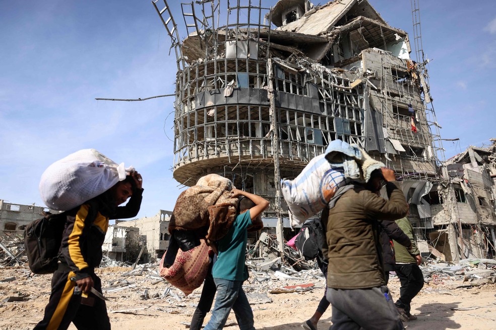 Palestinos deslocados carregam seus pertences enquanto caminham em meio à devastação ao retornarem para Rafah, no sul da Faixa de Gaza — Foto: AFP/Bashar Taleb