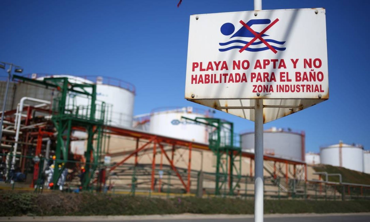 Placa alerta a população com a inscrição "Praia não adequada e não é habilitada para banho, zona industrial" perto da fábrica química de Oxiquim, cujo tubo vai para a praia de Las Ventanas — Foto: PABLO VERA / AFP