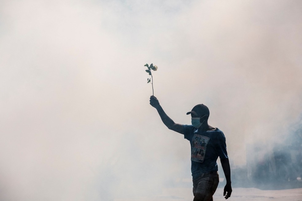 Manifestante segura uma flor em homenagem a vítima de protesto no Quênia em meio à fumaça de gás lacrimogêneo — Foto: Kabir Dhanji / AFP