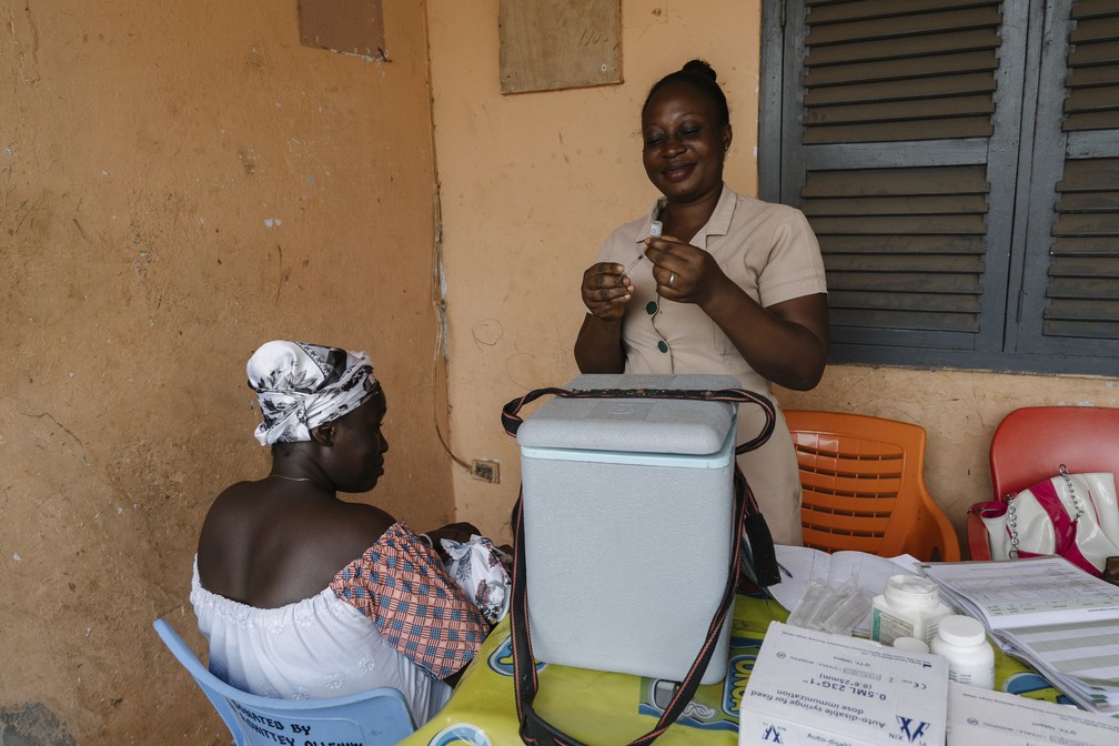 Deborah Sebi (em pé), enfermeira em uma clínica móvel em Teshie, uma vila de pescadores perto de Accra, Gana, preparando uma imunização para Doris, de 3 meses, filha de Rebecca Bamembaye, em julho de 2023 — Foto: Natalija Gormalova/The New York Times