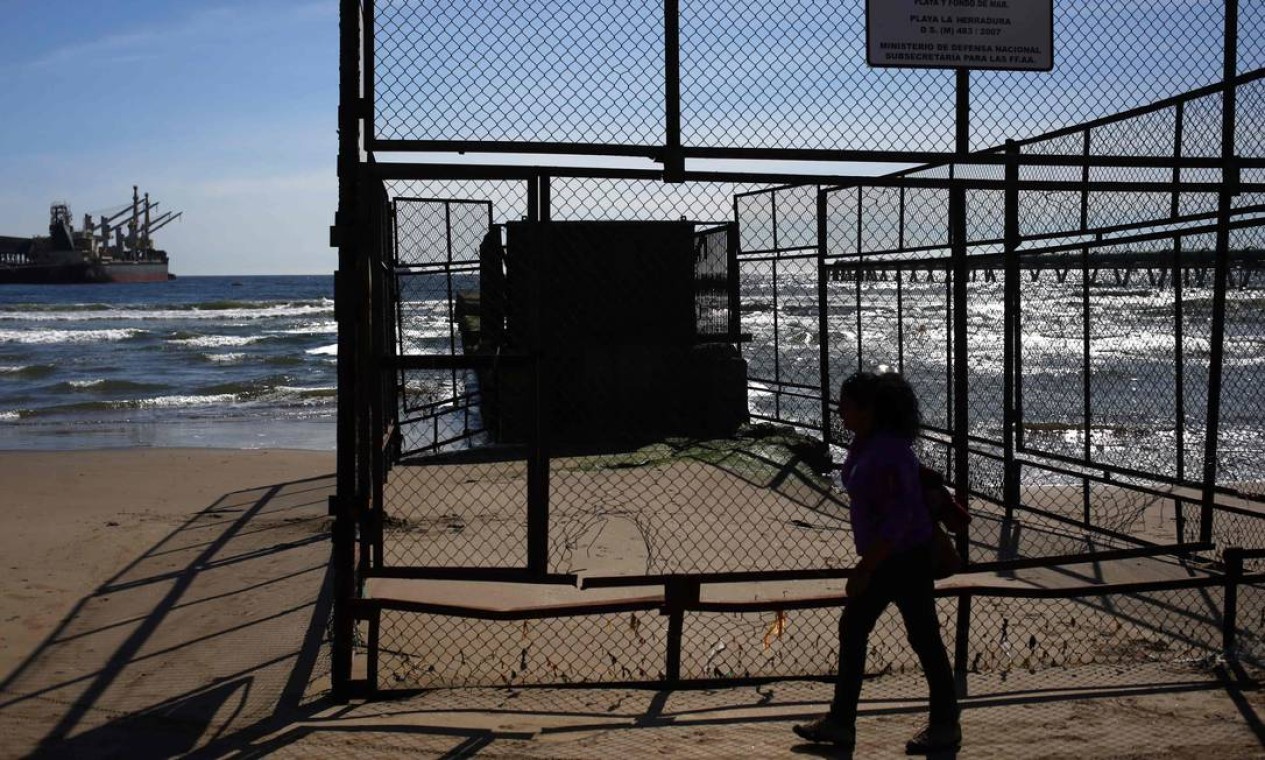 Uma mulher passa por dutos em Puerto Ventanas. Polo industrial abriga quatro termelétricas a carvão e refinarias de petróleo e cobre — Foto: PABLO VERA / AFP