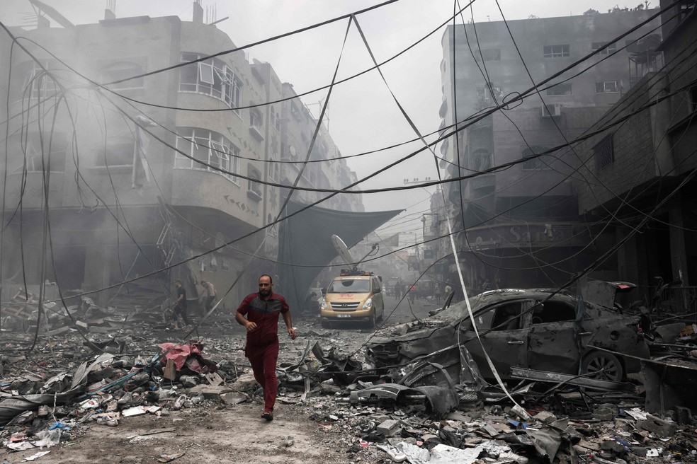 Palestino corre entre os escombros após ataque de Israel a centro de refugiados na Faixa de Gaza — Foto: Mohammed Abed / AFP