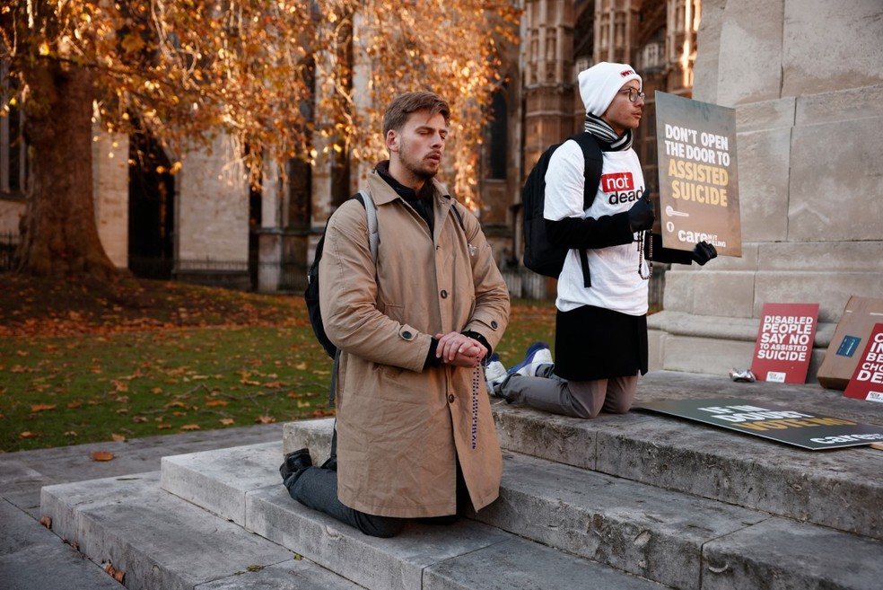 Manifestantes contrários ao projeto de lei do suicídio assistido se ajoelham em oração após a aprovação do projeto de lei para legalizar a eutanásia no Reino Unido — Foto: BENJAMIN CREMEL/AFP