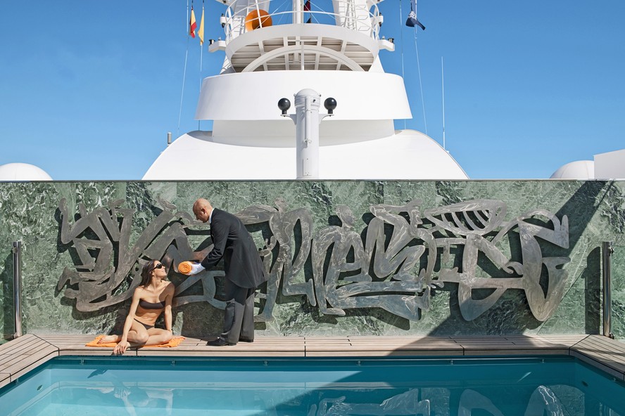 Mordomo leva uma toalha a uma hóspede na piscina exclusiva do Yacht Club, área VIP dos navios da MSC Cruzeiros