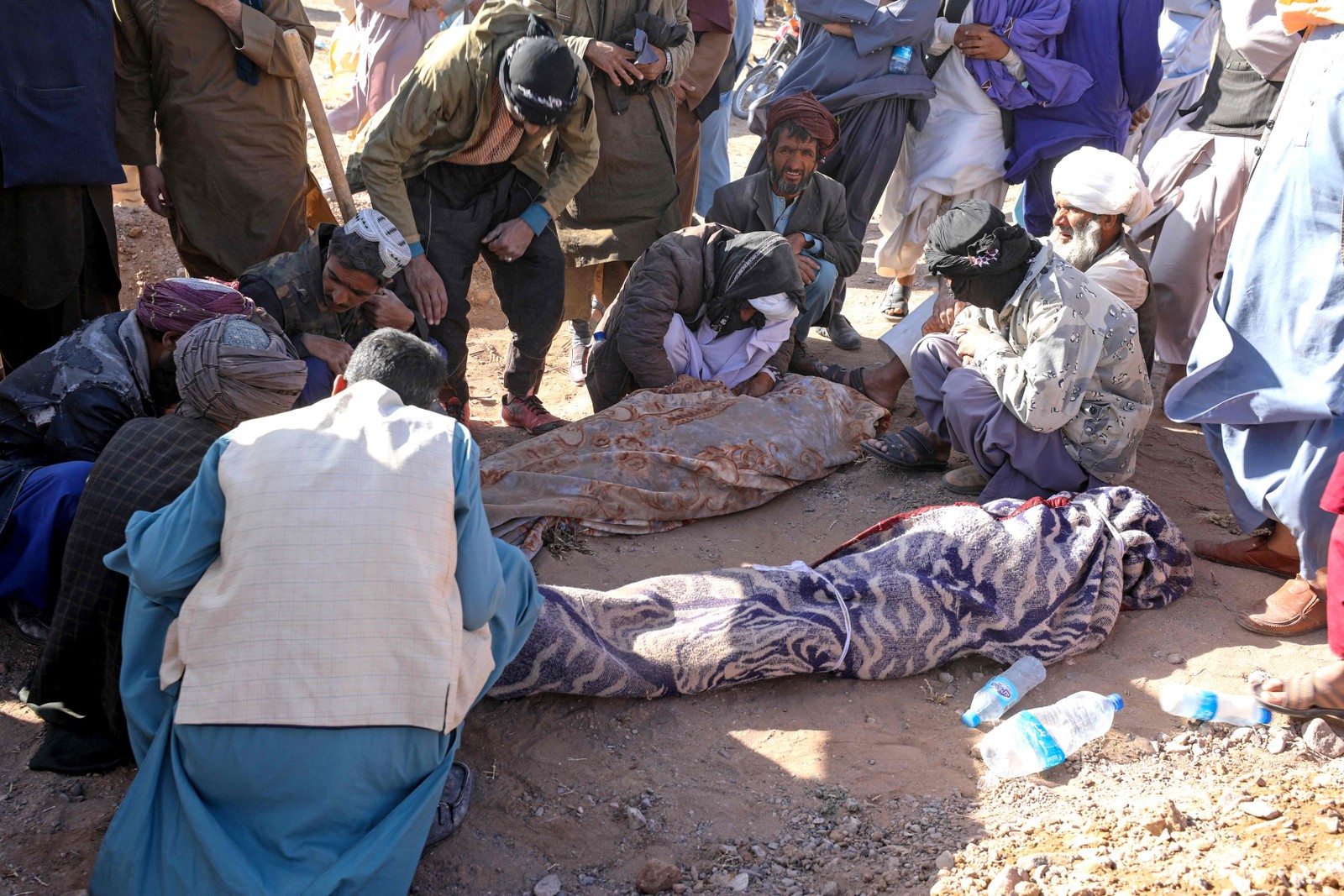 Afeg&atilde;os enlutados sentam-se ao lado dos corpos de seus parentes dos terremotos na vila de Sarbuland &mdash; Foto: Mohsen KARIMI / AFP