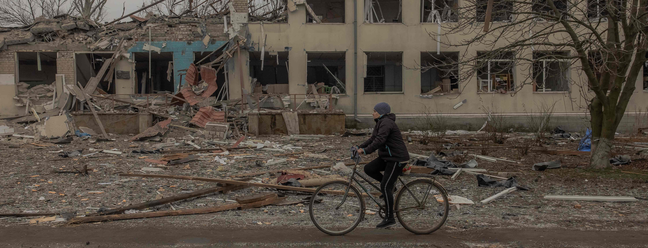 Mulher andando de bicicleta em meio a destroços após bombardeio na vila Novopavlivka, na Ucrânia — Foto: Roman PILIPEY / AFP