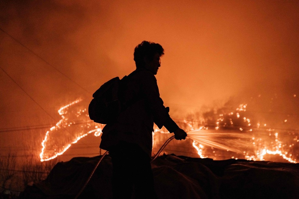 Mulher borrifa água em seus equipamentos agrícolas para evitar que eles queimem enquanto incêndios florestais são vistos em Uiseong, Coreia do Sul — Foto: AFP