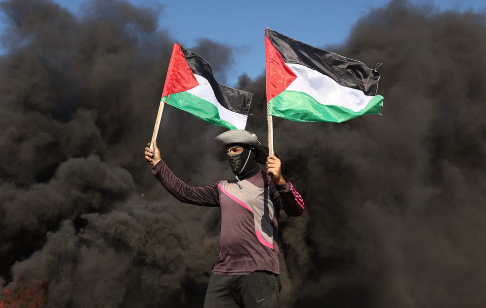 Jovem palestino carrega bandeiras durante protesto por operação militar israelense. — Foto: Mahmud Hams/AFP