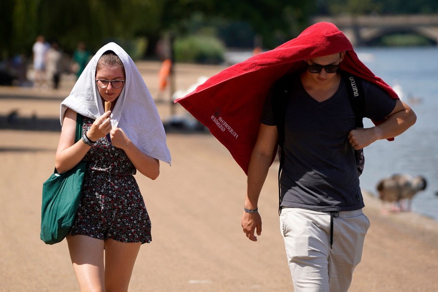 Pessoas caminham pelo Hyde Park, em Londres, com as cabeças cobertas para se protegerem do Sol