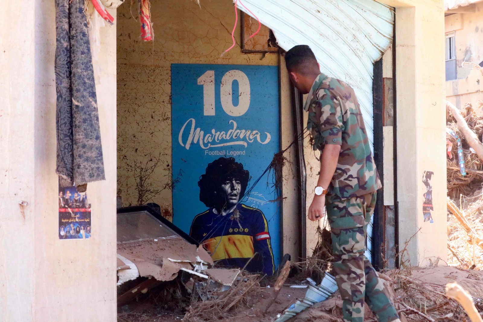 Um soldado olha para um pôster do falecido astro do futebol argentino Diego Maradona em meio às ruínas de uma casa destruída em enchentes na cidade de Derna — Foto: Abdullah DOMA/AFP
