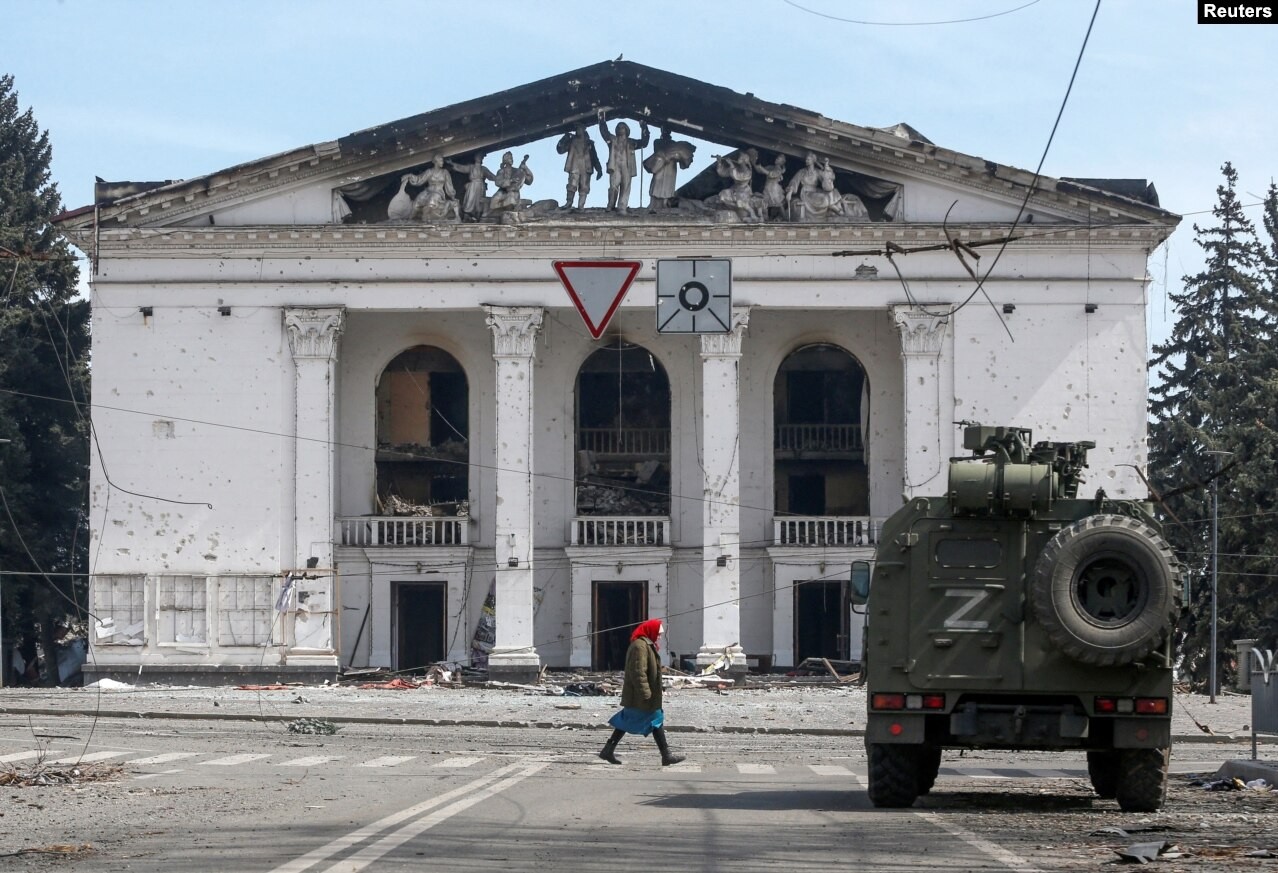 Idosa passa em frente ao teatro destruído e um veículo blindado das forças pró-Rússia, em abril de 2022  — Foto: Reuters