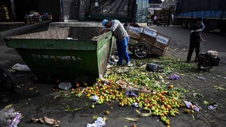 Um homem procura comida dentro de uma lata de lixo onde frutas e vegetais descartados são depositados no Mercado Central de Buenos Aires. — Foto: Luis ROBAYO / AFP