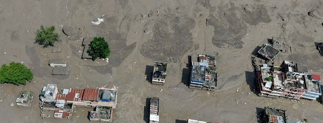 Casas ficam parcialmente submersas em água barrenta ao longo da margem de um rio após inundações — Foto: Prabin RANABHAT / AFP