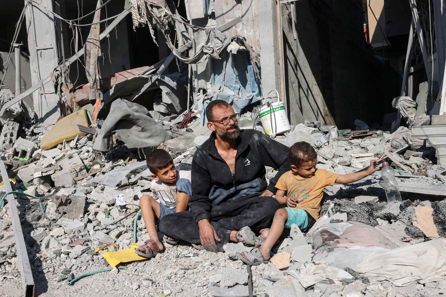 Pai palestino com seus filhos em destroços na Faixa de Gaza, após bombardeio de Israel