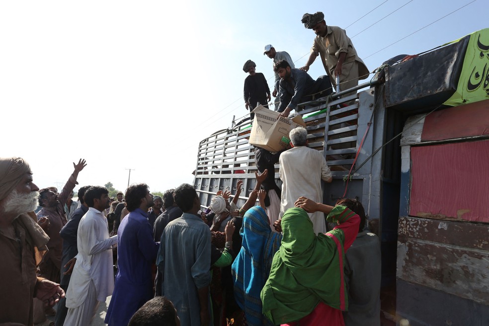 Na província de Punjab, desabrigados sobem em um caminhão para pegar caixas de comida distribuídas por equipes de socorro — Foto: Shahid Saeed MIRZA/AFP