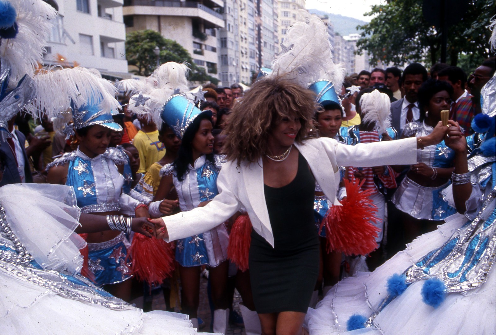 Tina Turner dança com integrantes da Escola de Samba Beija-Flor, que realizou uma homenagem em frente ao hotel onde a cantora estava hospedada, em Copacabana, em 1987  — Foto: Hipólito Pereira / Agência O Globo