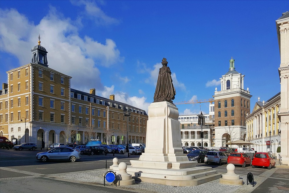A Queen Mother Square, a praça central do povoado de Poundbury, com a estátua em homenagem à avó de Charles III — Foto: Reprodução / Wikimedia Commons