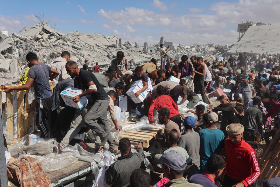 Palestinos recolhem pacotes de ajuda em caminhões que entraram pela passagem de Karem Abu Salem, em Khan Younis, no sul da Faixa de Gaza — Foto: Omar al-Qattaa/AFP