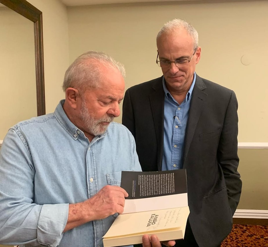 O presidente Lula em discurso com expressão séria e, ao lado, o senador Flávio Bolsonaro em evento político, representando o confronto eleitoral de 2026.