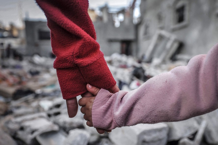Pessoas de mãos dadas em meio à destruição em Rafah, no sul da Gaza, após as batalhas entre Israel e Hamas
