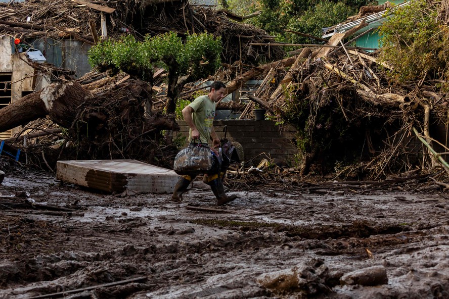 Um homem caminha com seus pertences por uma rua coberta de lama e detritos após passagem de ciclone em Muçum, Rio Grande do Sul