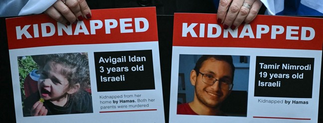 Manifestantes seguram fotos de Avigail Idan, de 3 anos, e Tamir Nimrodi, 19, mantidos reféns pelo Hamas em Gaza, durante uma manifestação em frente a Downing Street, em 19 de novembro de 2023, para protestar contra o antissemitismo e pedir a libertação dos reféns. — Foto: JUSTIN TALLIS / AFP