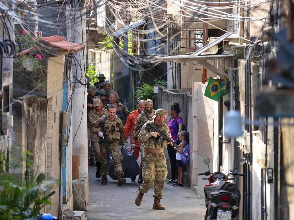 Mulher cobre o rosto de criança durante a passagem de policiais com o corpo de suspeito morto em operação na Ladeira dos Tabajaras — Foto: Márcia Foletto / Agência O Globo
