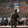 Um soldado espanhol observa migrantes sentados no chão antes de escoltá-los de volta ao Marrocos, no enclave espanhol de Ceuta, no norte da África, em 1º de agosto de 2026 - JORGE GUERRERO / AFP