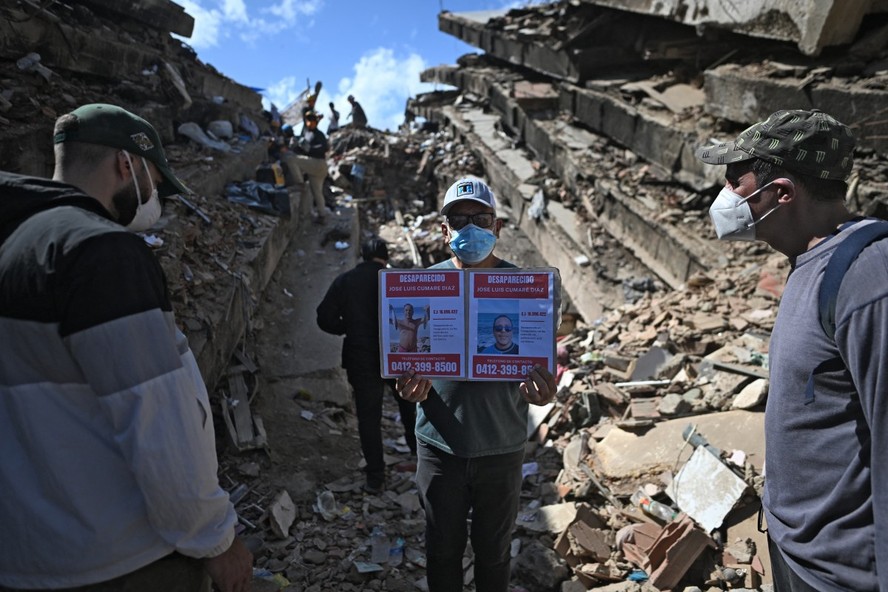 Um homem mostra fotos de pessoas desaparecidas em meio aos escombros na praia de Los Cocos, em Caraballeda, estado de La Guaira, Venezuela, em 1&ordm; de julho de 2026, ap&oacute;s os dois terremotos ocorridos em 24 de junho