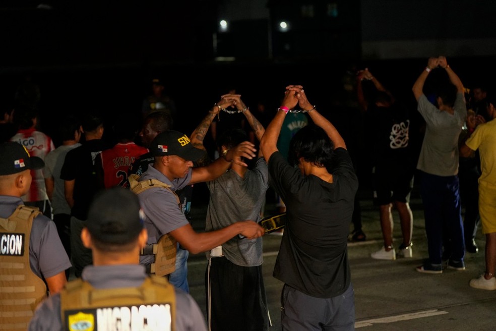 Migrantes colombianos algemados fazem fila no aeroporto Albrook Gelabert, na Cidade do Panamá, em 20 de agosto de 2024, enquanto são examinados com detectores de metais antes de sua deportação — Foto: ARNULFO FRANCO/AFP