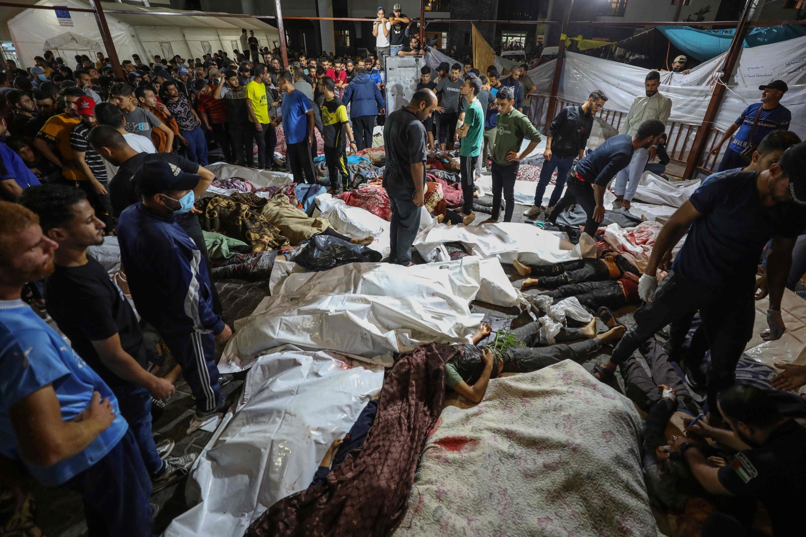 Pessoas se reúnem em torno de corpos de palestinos mortos em ataques aéreos israelenses no hospital Ahli Arab, no centro de Gaza — Foto: Dawood NEMER/AFP