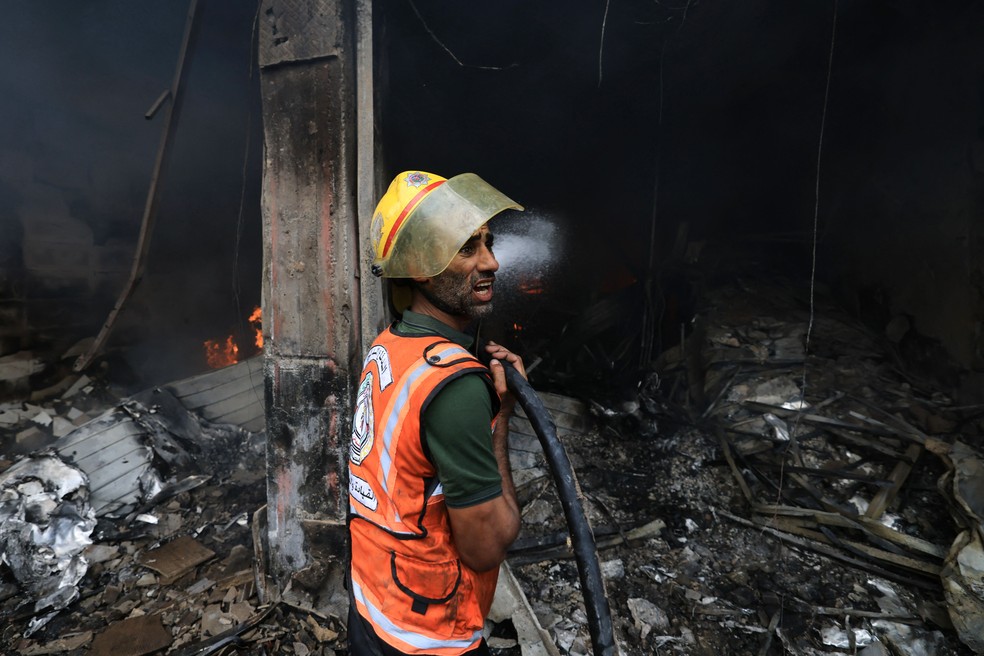 Bombeiro palestino apaga fogo causado por ataque de Israel a centro de refugiados na Faixa de Gaza — Foto: Mahmud Hams / AFP