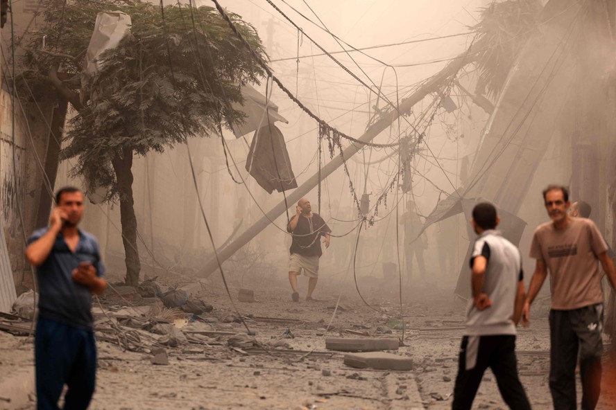 Palestinos percorrem bairro fortemente danificado por ataques aéreos israelenses na cidade de Gaza