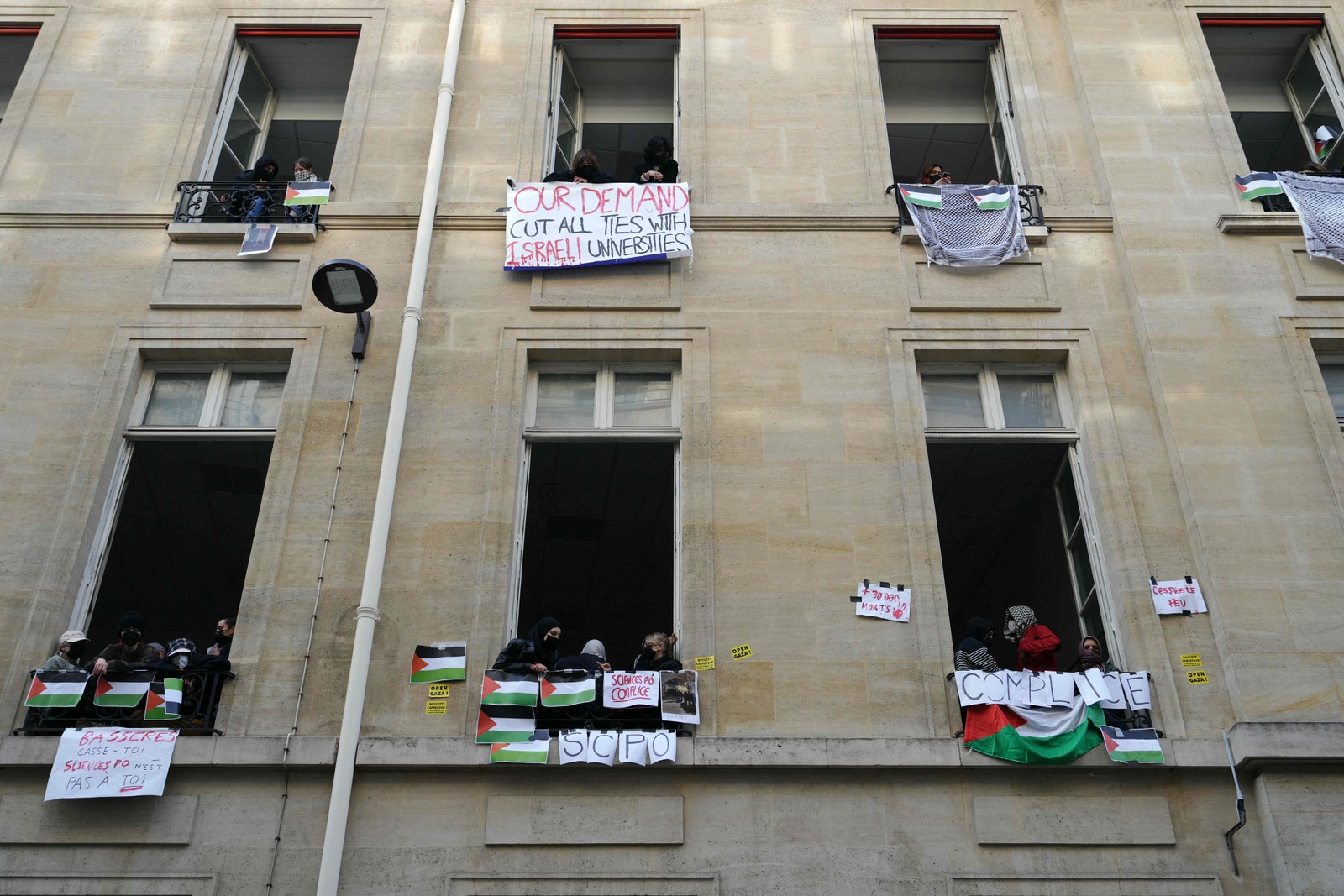 Manifestantes olham pelas janelas durante a ocupação de um prédio do Instituto de Estudos Políticos (Sciences Po Paris) por estudantes em apoio aos palestinos, com uma barricada bloqueando a entrada, em Paris — Foto: Dimitar DILKOFF / AFP