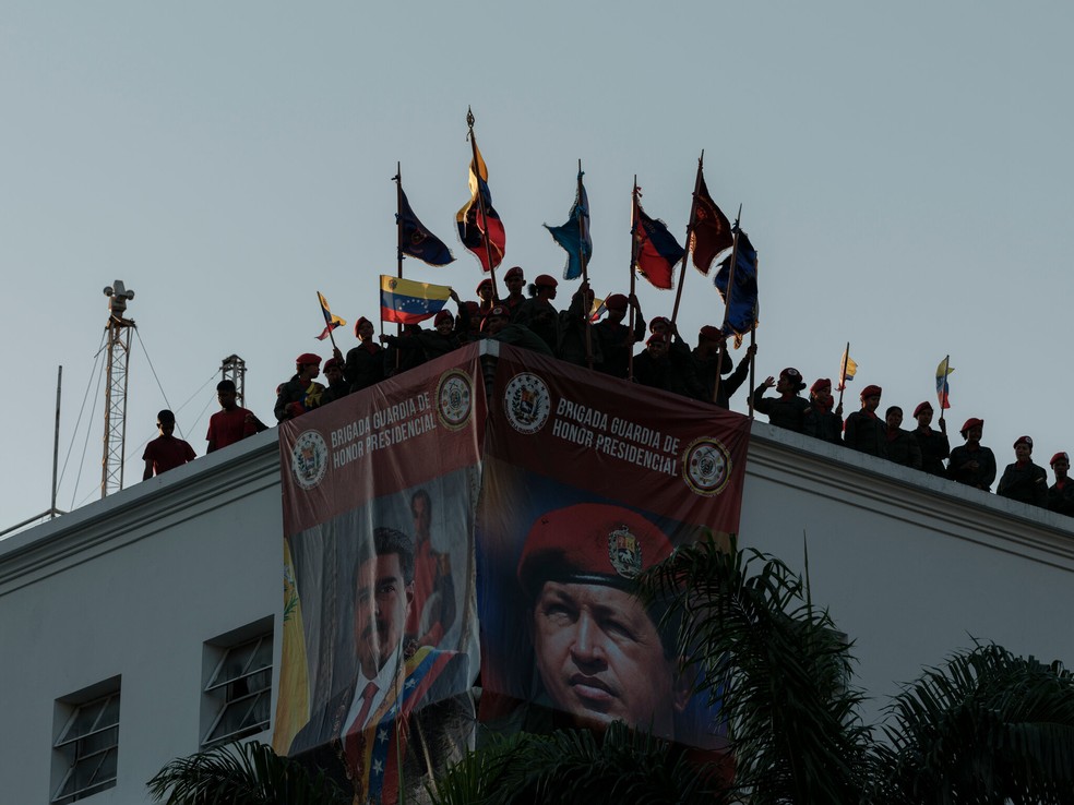 Soldados segurando bandeiras no telhado de um prédio militar em Caracas, no ano passado, durante uma manifestação em apoio ao governo — Foto: Alejandro Cegarra/The New York Times