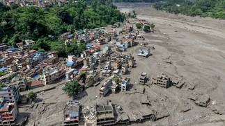 Casas ficam parcialmente submersas em água barrenta ao longo da margem de um rio — Foto: Prabin RANABHAT / AFP