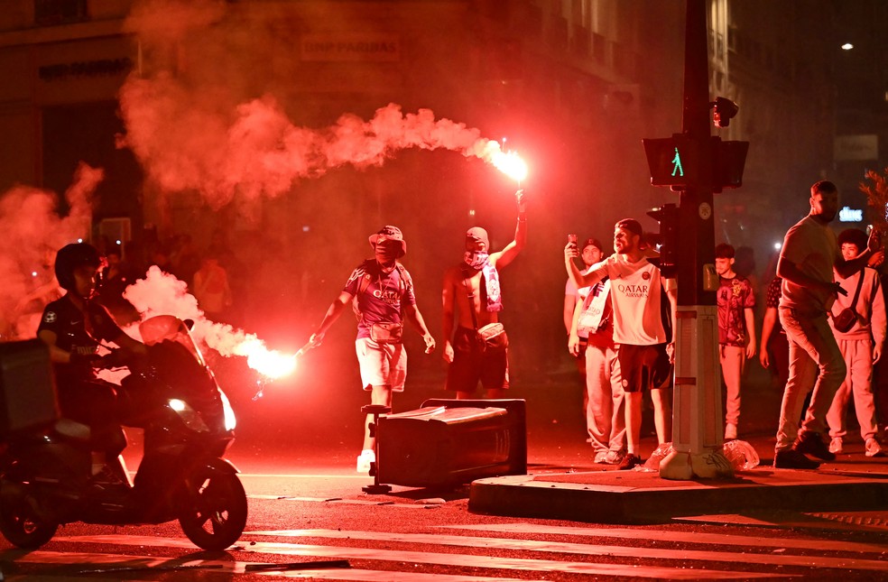 Torcedores do Paris Saint-Germain (PSG) se reúnem segurando sinalizadores em uma rua de Paris — Foto: LOU BENOIST / AFP