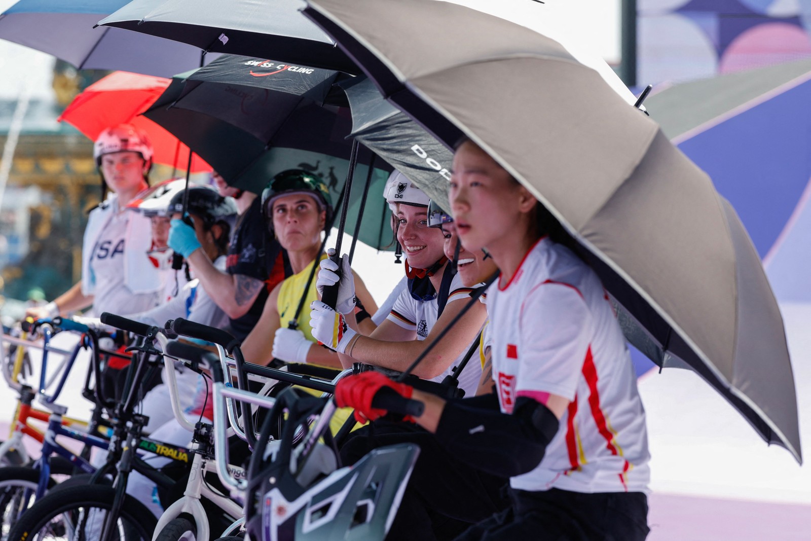 Cyclists protect themselves from the sun with umbrellas before the start of the women's BMX Freestyle Park cycling qualification — Photo: Odd Andersen / AFP