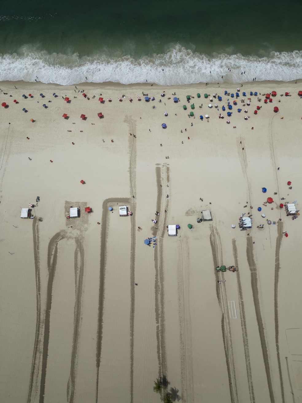 Barraqueiros fazem trilhas de água na areia para que as pessoas consigam caminhar até as barracas sob o sol — Foto: Márcia Foletto/Agência O Globo