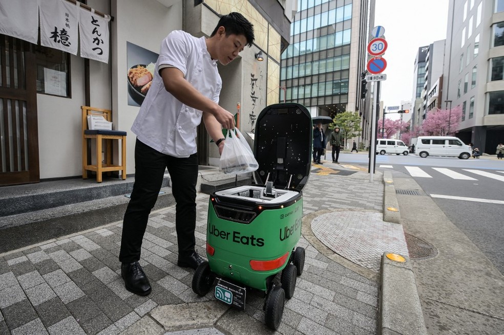 Funcionário de restaurante entrega um pedido para um robô durante uma demonstração do serviço de entrega da Uber Eats Japan — Foto: Richard A. Brooks / AFP