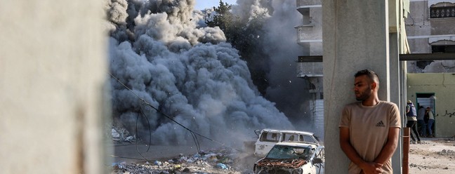 Um homem se protege atrás de uma coluna enquanto uma explosão propaga fumaça e poeira durante um ataque israelense que supostamente teve como alvo uma escola no distrito de Zeitoun, nos arredores da Cidade de Gaza, em 1º de setembro de 2024 — Foto: Omar AL-QATTAA / AFP