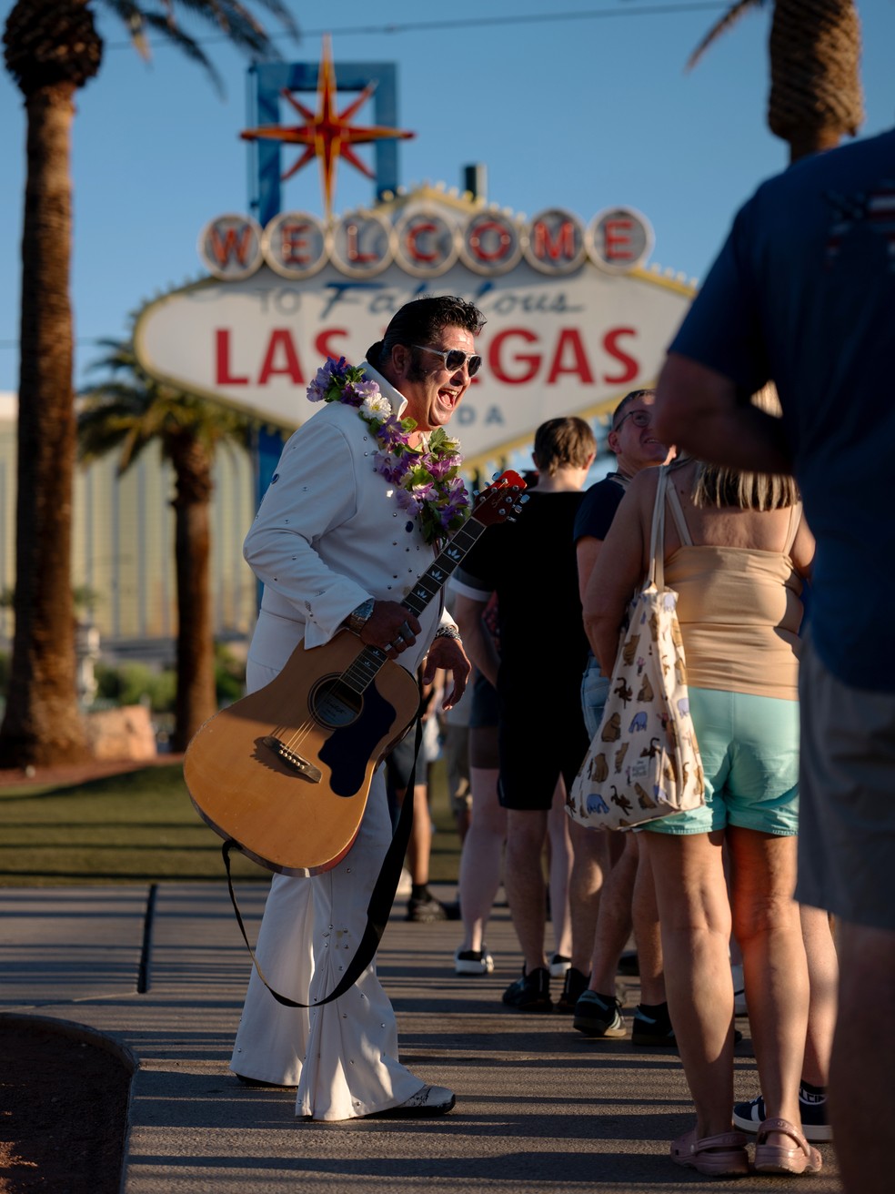 Mark Rumpler, imitador de Elvis, conversa com turistas perto da placa histórica que lhes dá as boas-vindas a Las Vegas, nos EUA — Foto: Tag Christof/The New York Times