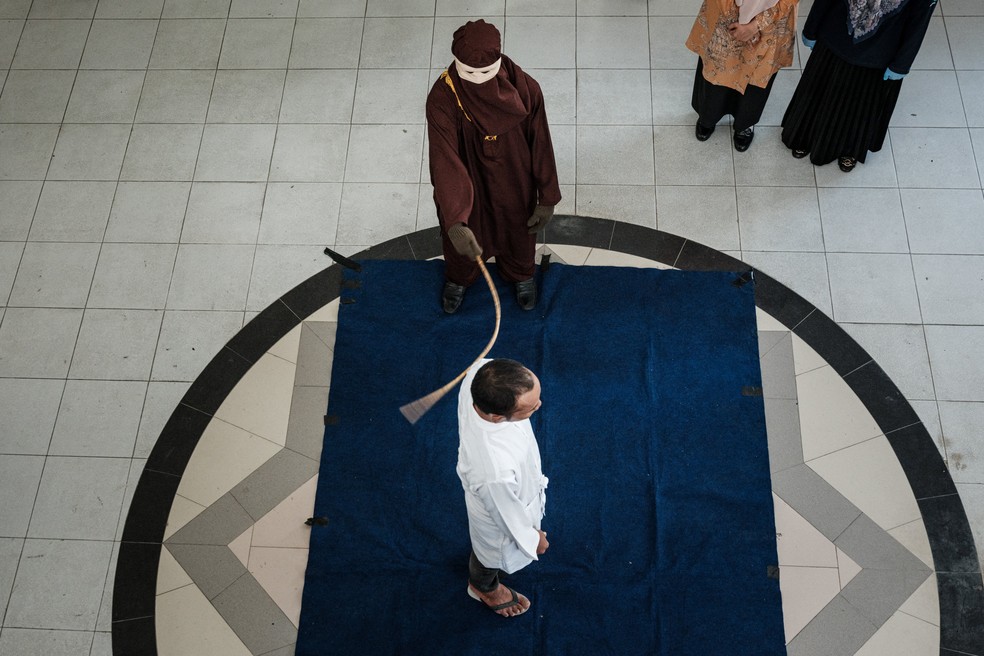 Um membro da polícia da Sharia açoita um homem considerado culpado de relações sexuais com outro homem sob a estrita lei islâmica da sharia — Foto: YASUYOSHI CHIBA / AFP
