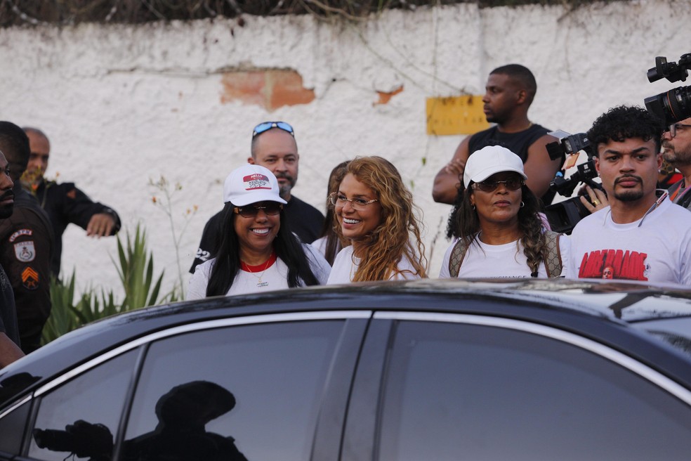 A noiva (loira de óculos sorrindo) a mãe e o irmão de Oruam após a saída do cantor em Gericinó — Foto: Júlia Aguiar