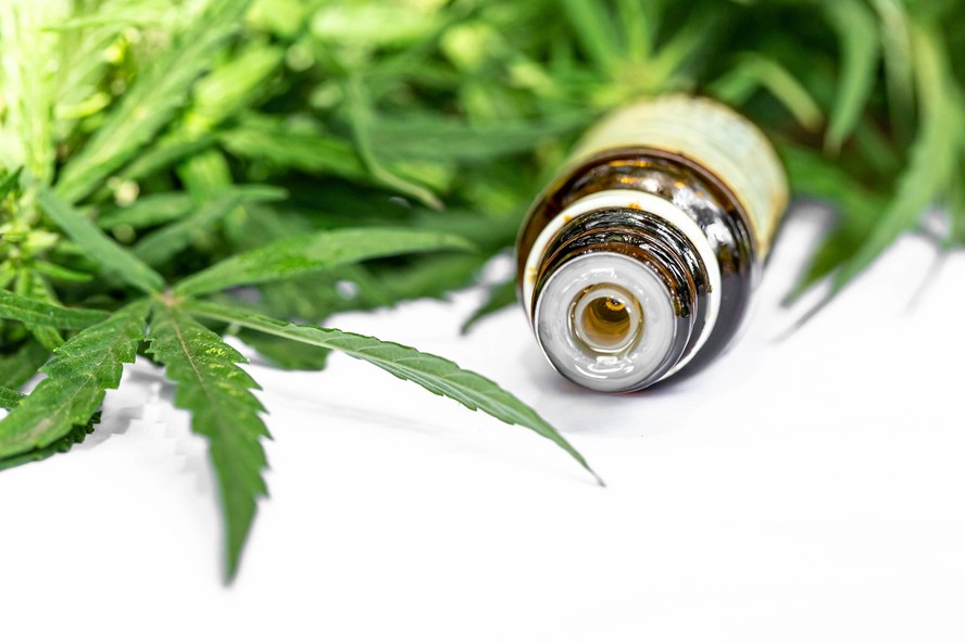 Frasco de óleo de cannabis medicinal ao lado de folha da planta