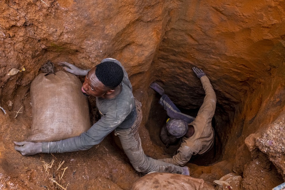 Homens transportam sacos de cobalto bruto de um buraco cavado à mão na mina artesanal de Kasulu, na RDC — Foto: Ashley Gilbertson/The New York Times